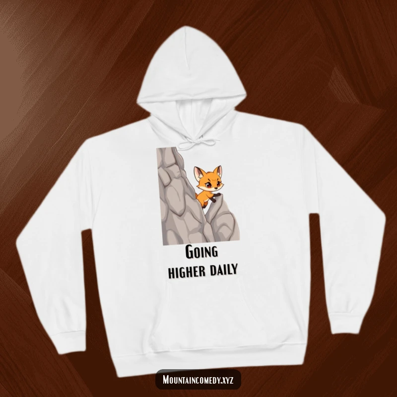 Funny fox cub character scaling a steep cliff with confidence, depicted on a warm and motivational hoodie for adventurers.